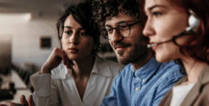 3 IT technicians looking at their desktop computers. They are wearing headsets